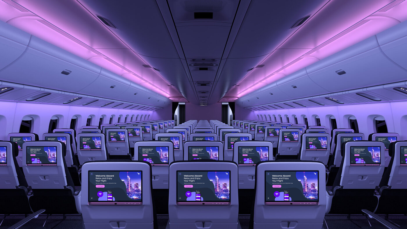 Aircraft cabin interior showing rows of seatback displays with HDR10+ compatible screens showing a welcome message, under ambient purple cabin lighting
